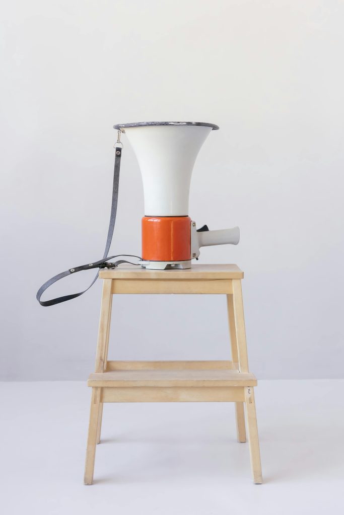 A red and white megaphone placed on a wooden stool against a minimalist background.
